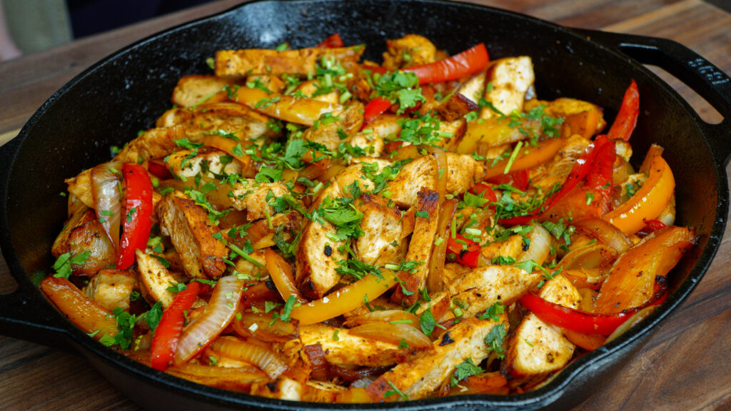 Chicken fajitas in a cast iron pan, ready to be served and sprinkled with fresh cilantro.