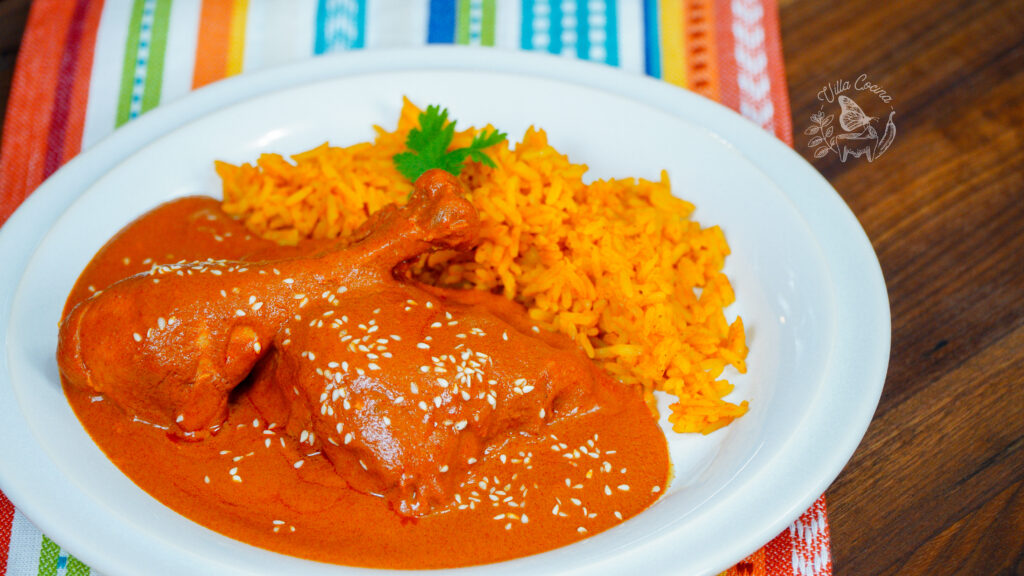 chicken mole rojo served in a white plate along with mexican rice
