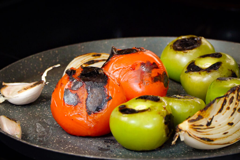 tomatoes, tomatillos, onion, and garlic being roasted on a comal for a salsa.