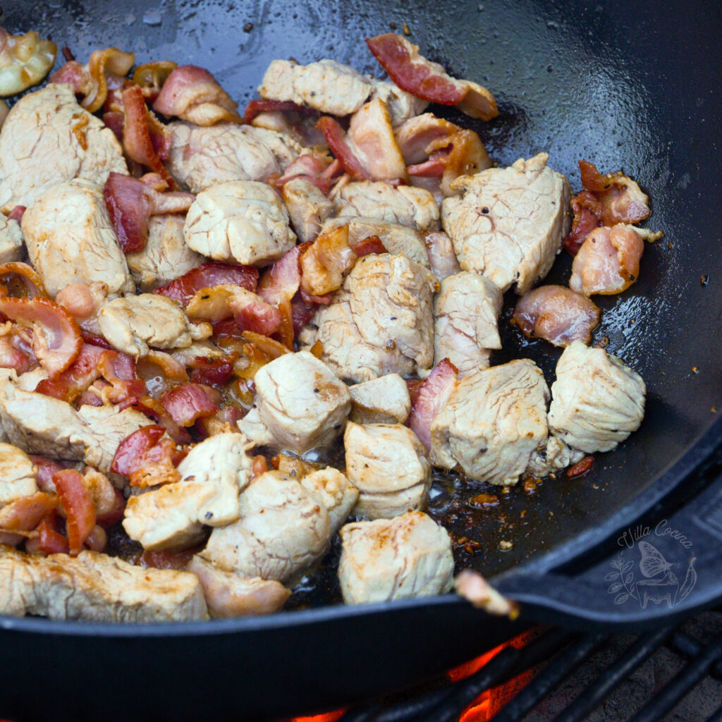 pork loin being cooked on a weber wok along with bacon