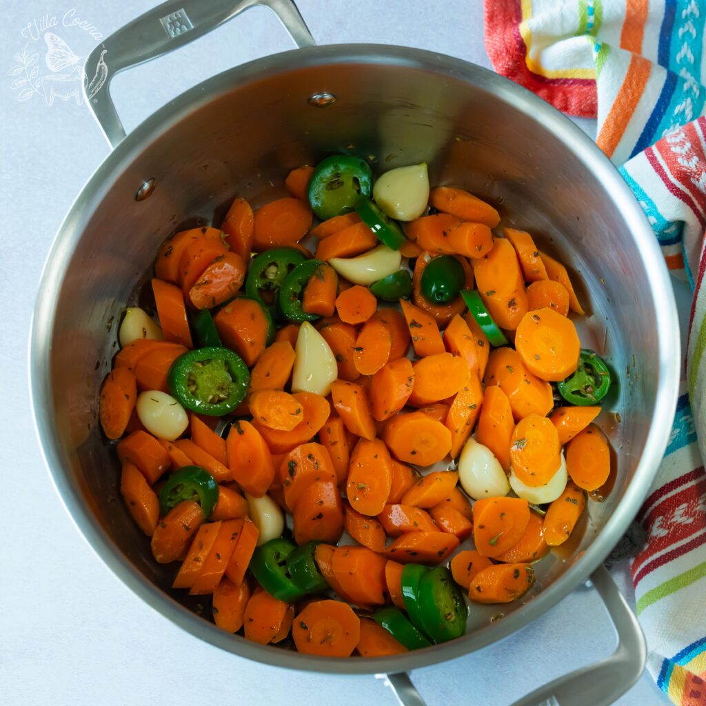 Chopped carrots, jalapeños, and garlic inside a pot and pre-cooking.