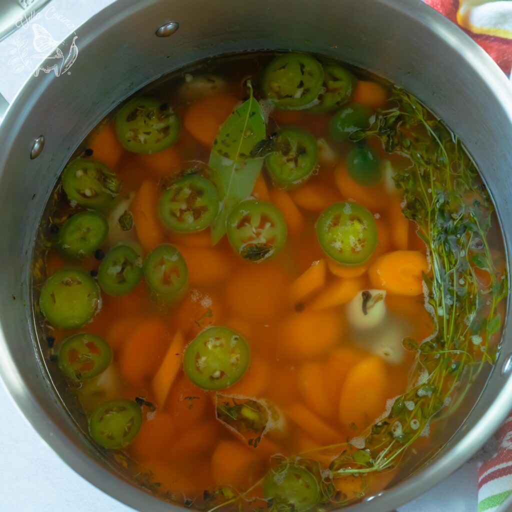 Chopped carrots, jalapeños, and garlic precooking inside a pot.