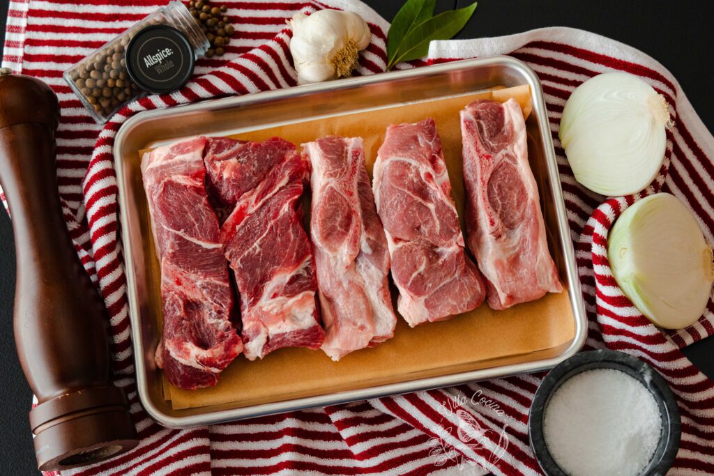 Pork ribs surrounded by salt, onion, bayleaves, garlic, allspice, and black pepper.