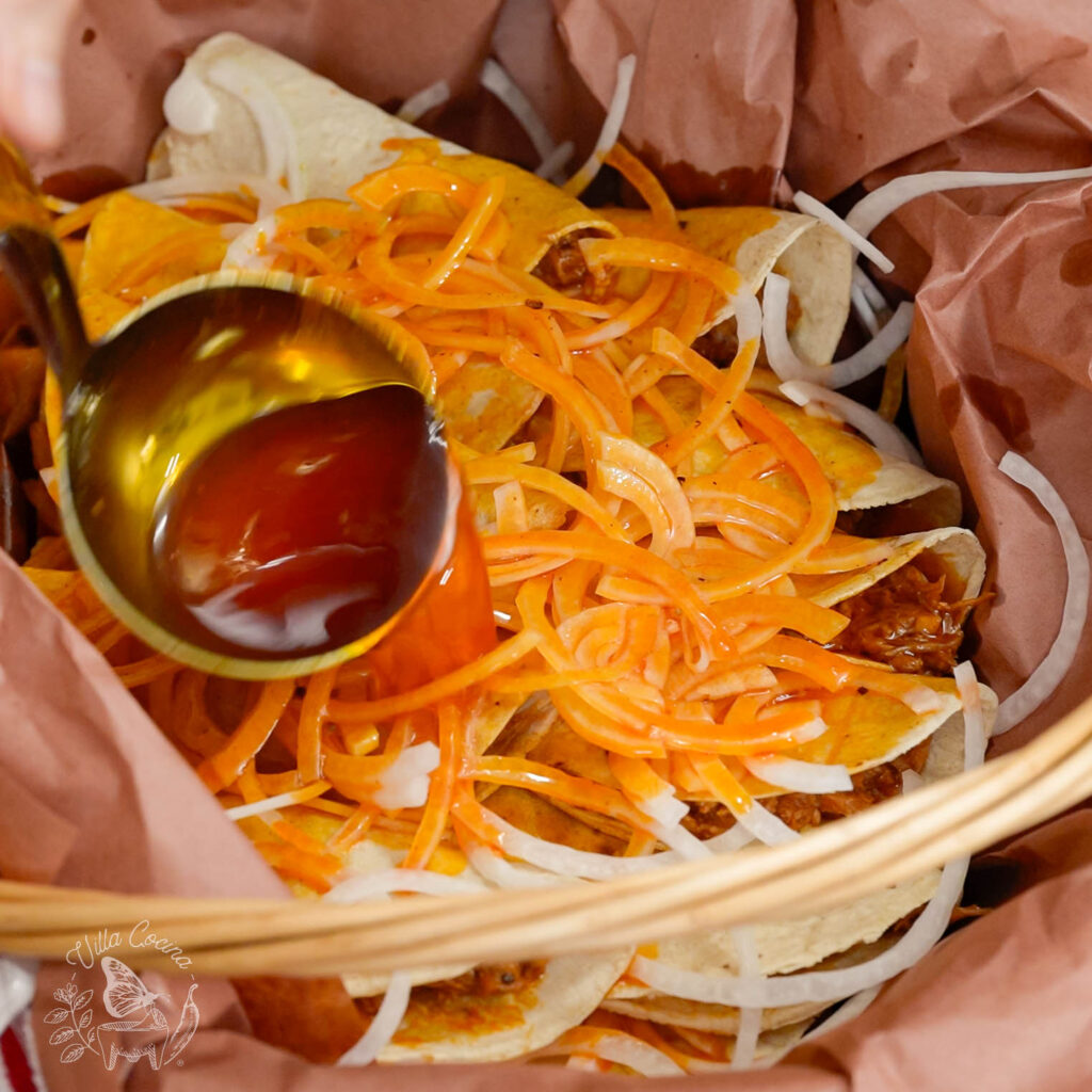 Tacos de canasta being drenched in a traditional Chile flavored oil.