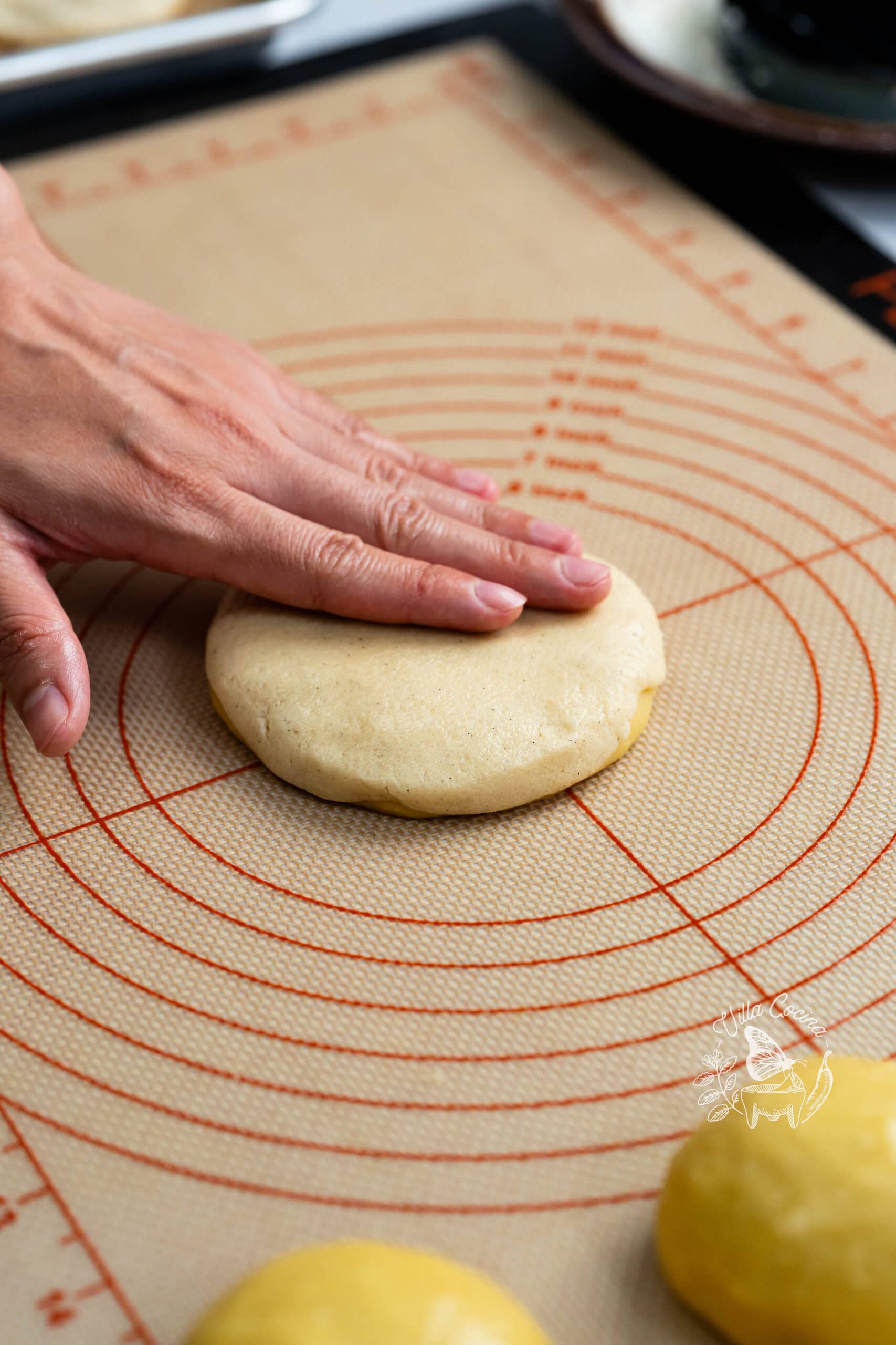 Hand gently flattening concha dough covered with vanilla topping.