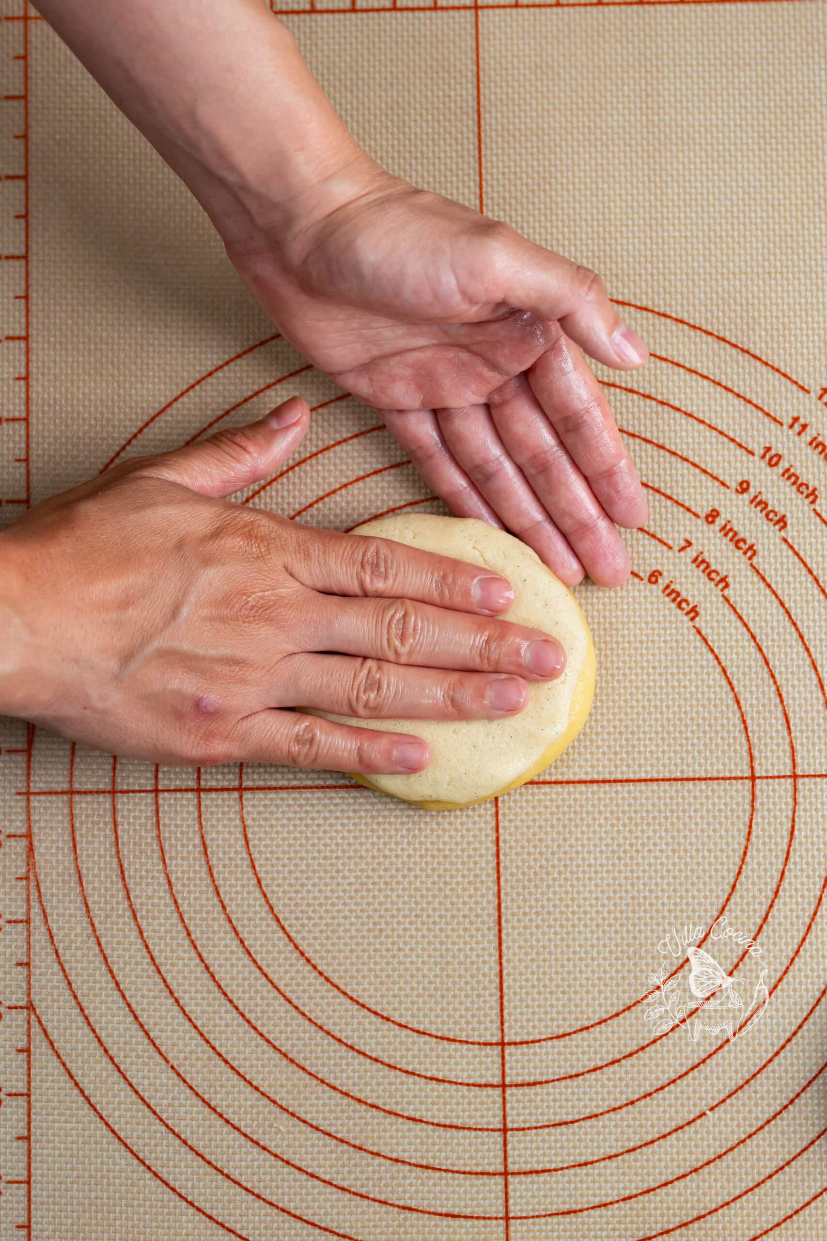 Hands smoothing vanilla sugar topping over concha dough.