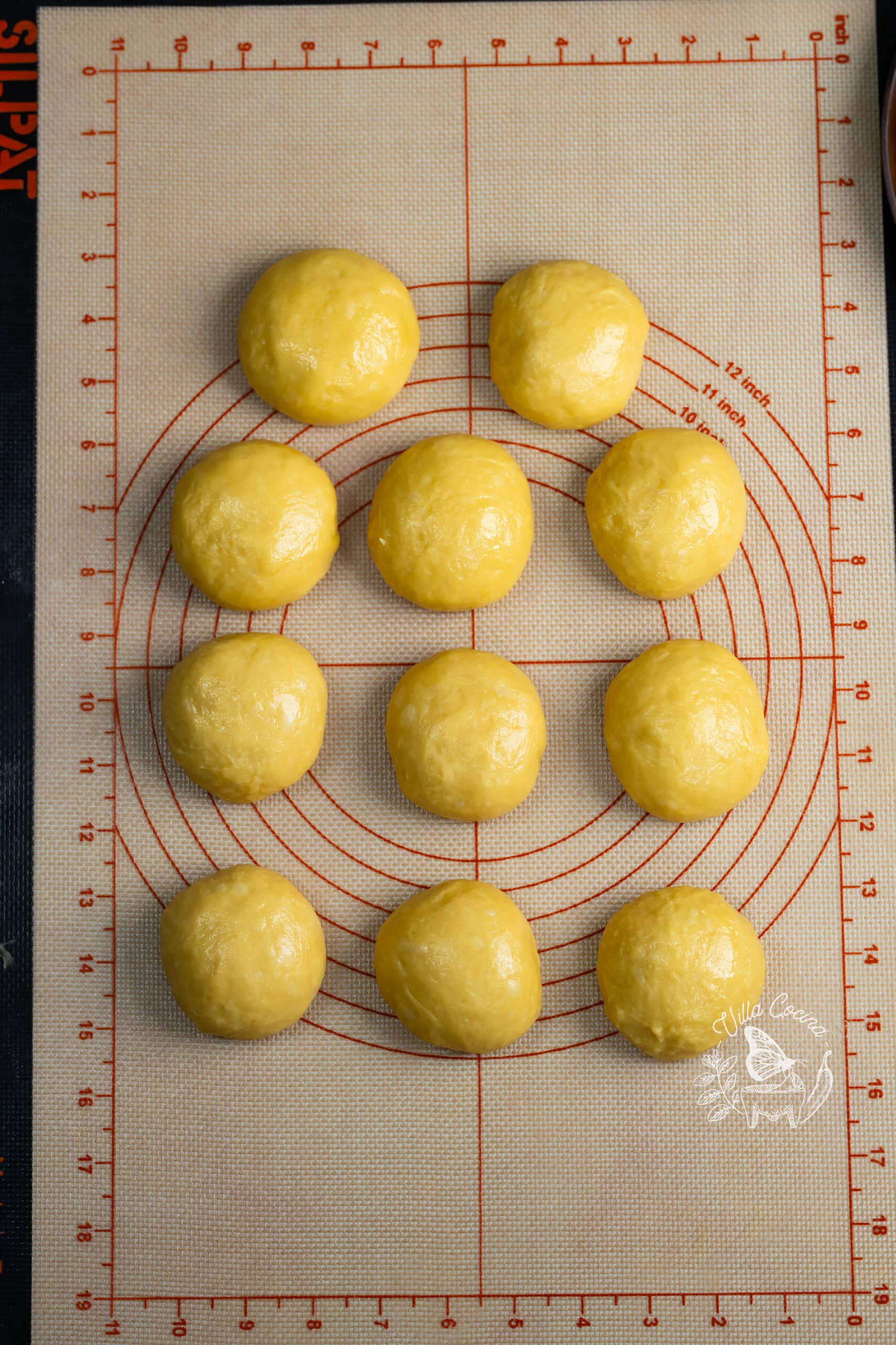 Eleven shaped concha dough balls on a silicone mat.