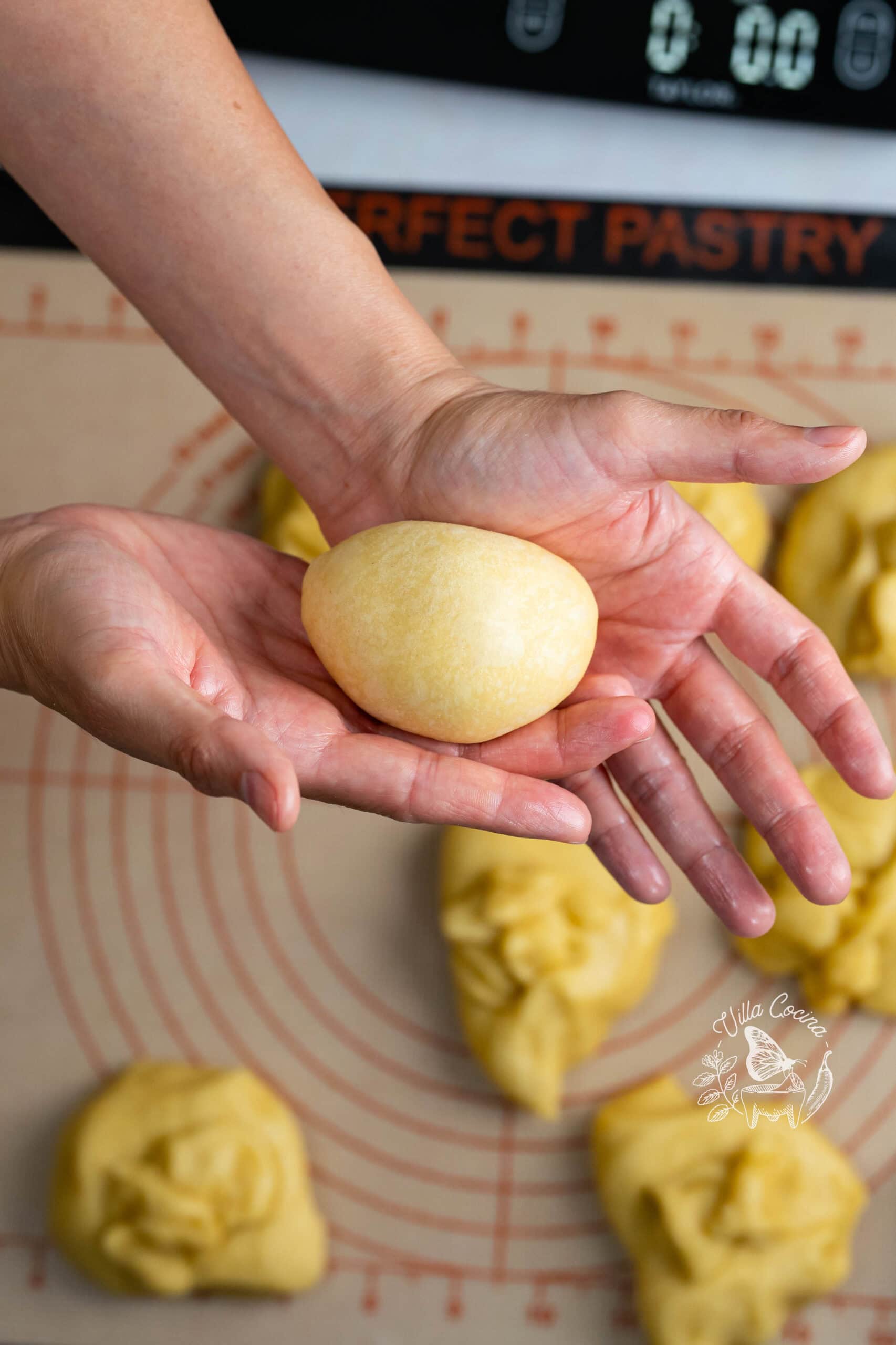 Hands shaping concha dough into a smooth, round ball.