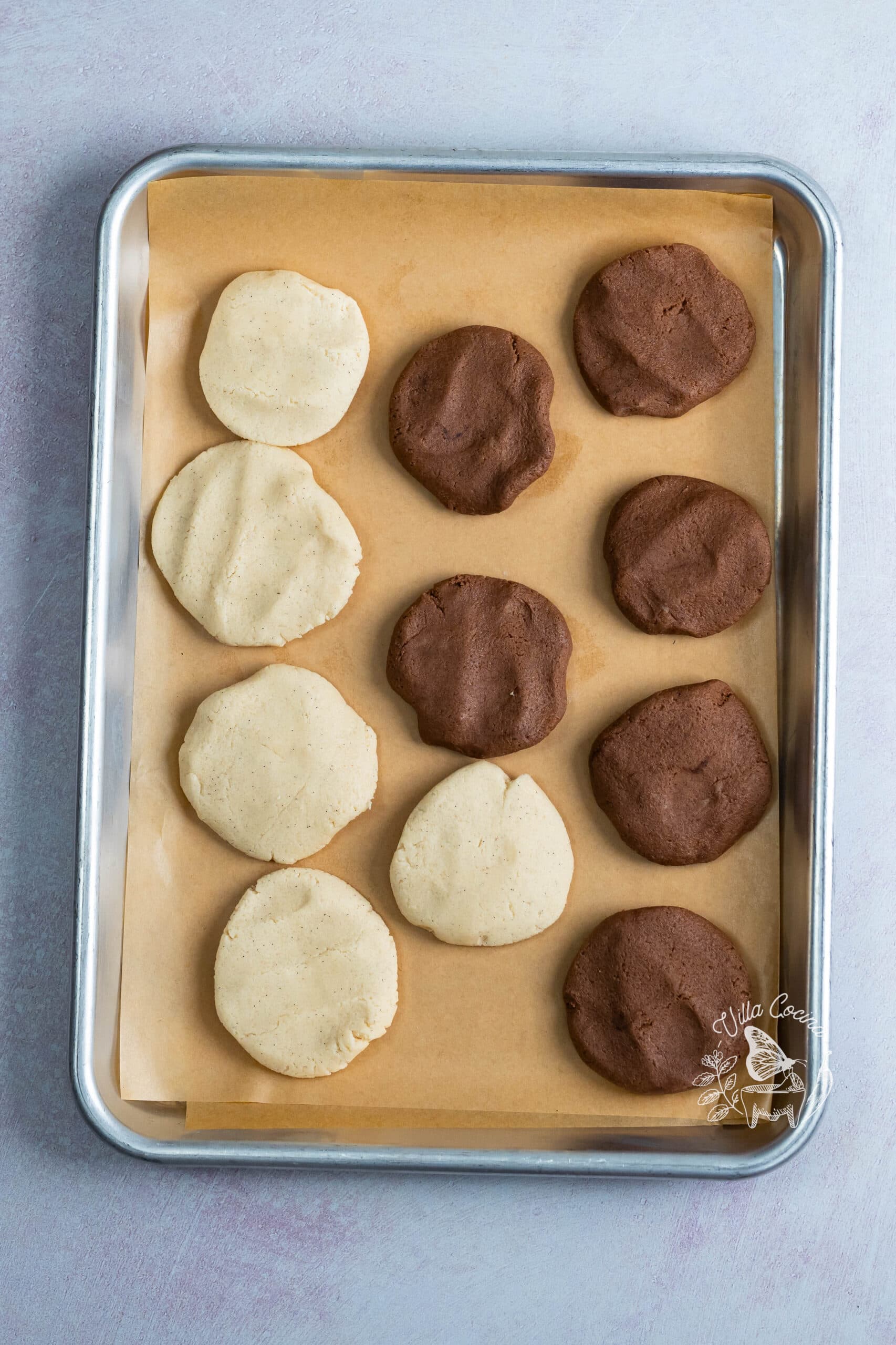 Flattened vanilla and chocolate topping portions on a parchment lined sheet pan.