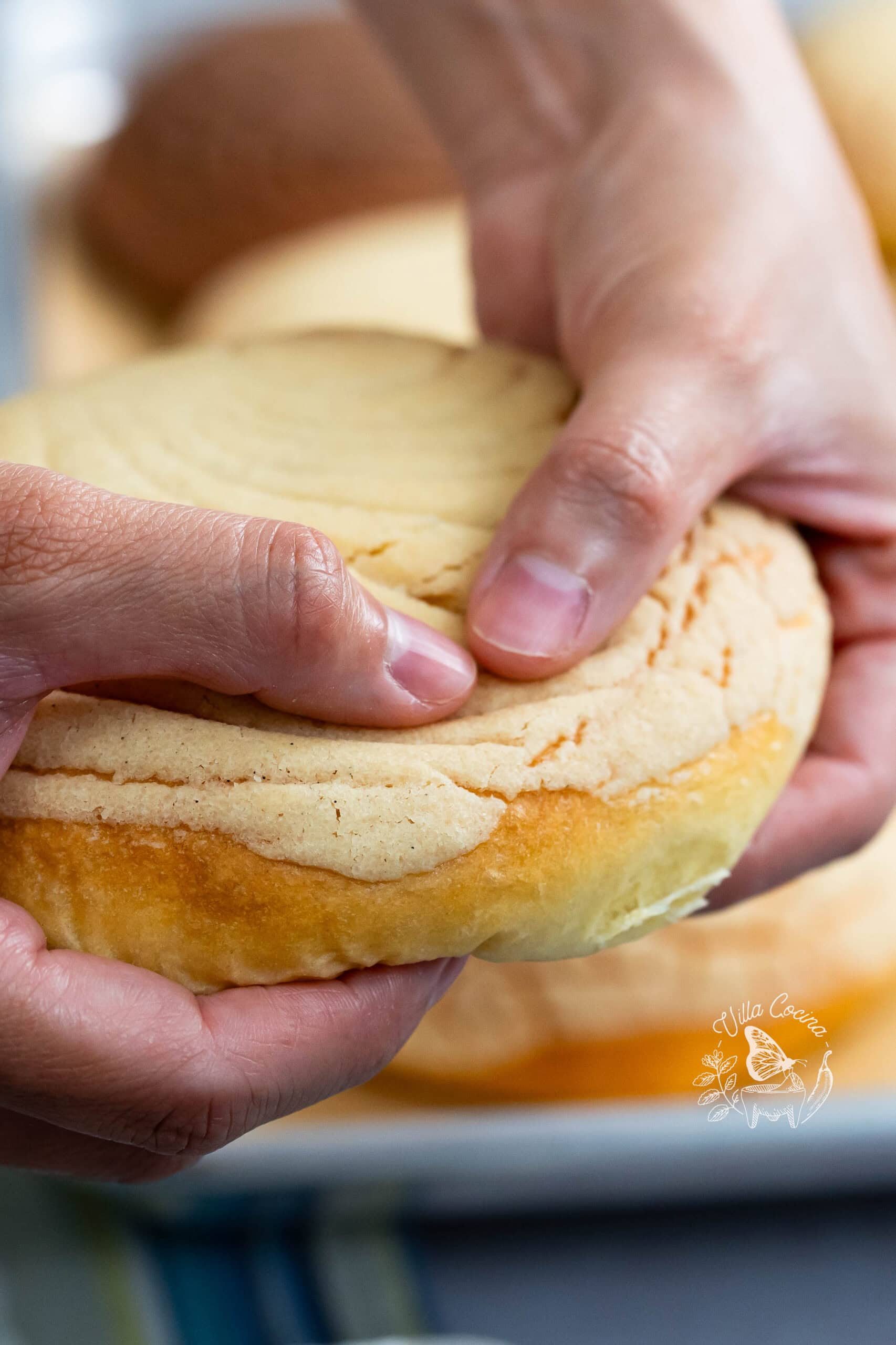 Hands gently pressing a soft Mexican concha with vanilla sugar topping.